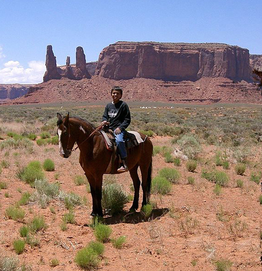 A young Navajo boy rides his horse in Monument Valley. The Navajo Nation includes much of the Four Corners area, including the valley, famous from many Western movies. Courtesy Wikimedia Commons.