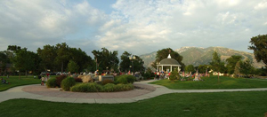 Draper Historic Park after the Draper Days Children's Parade. A magician is performing from the Gazebo, and the Wasatch mountains are in the background. Stitch of two photos taken by Scott Catron on July 15, 2008. Photo courtesy of author; accessed through Wikimedia Commons.