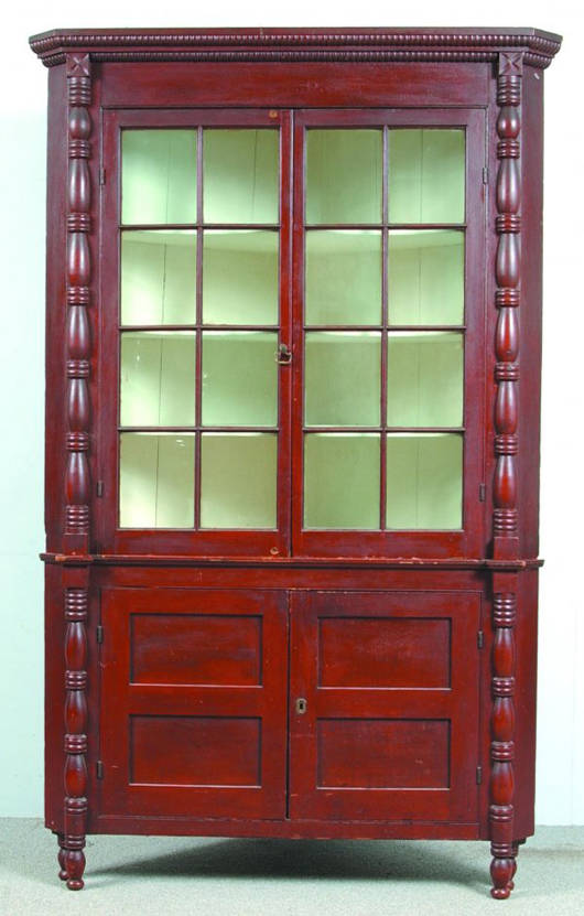 Old red paint covers this Pennsylvania country Sheraton Softwood two-part corner cupboard. It measures 88 1/4 inches high, 55 inches wide and 30 inches deep. It has a $3,000-$5,000 estimate. Image courtesy of Conestoga Auction Co.