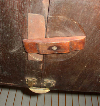 This view from under table shows the leaf in place, the turn button extended and the brass table fork in place at the bottom.