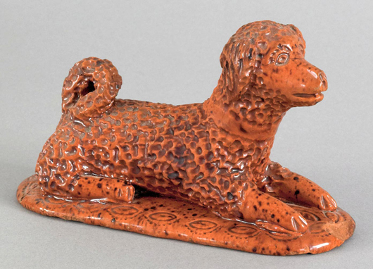 Pennsylvania redware figure of a reclining dog, mid 19th century, the base with impressed leaf border, 3 inches high x 5 inches wide. Est. $1,500-$2,500. Image courtesy of Pook & Pook Inc.