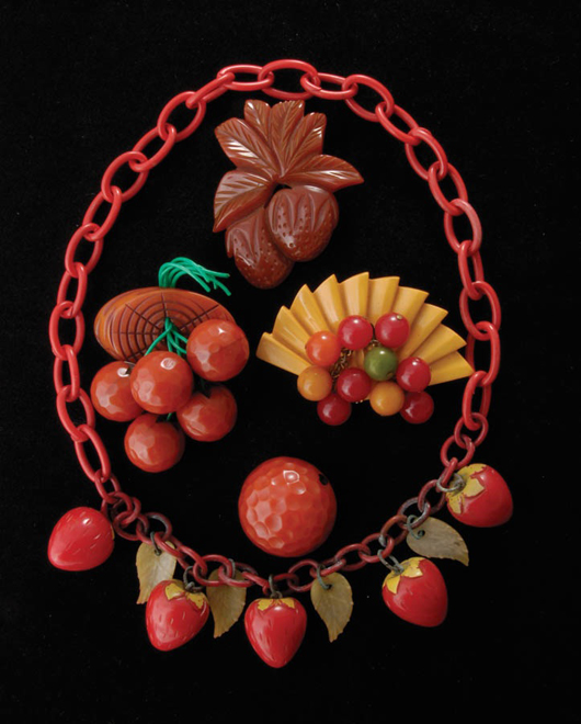 Carmen Miranda-inspired Bakelite consisting of a carved strawberry necklace, a carved strawberry pin, a carved pin with five carved oranges, an orange peel pin, and a fan-shape pin with multicolor drop berries. Estimate: $800-$1,200. Image courtesy of Michaan’s Auction.