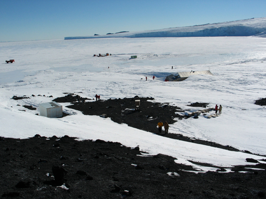 Nov. 8, 2003 photo of Cape Evans, Antarctica, in which Scott’s Hut can be seen buried in snow at center right. The Barne Glacier is visible in the background. Source: Antarctic Photo Library, U.S. Antarctic Program.
