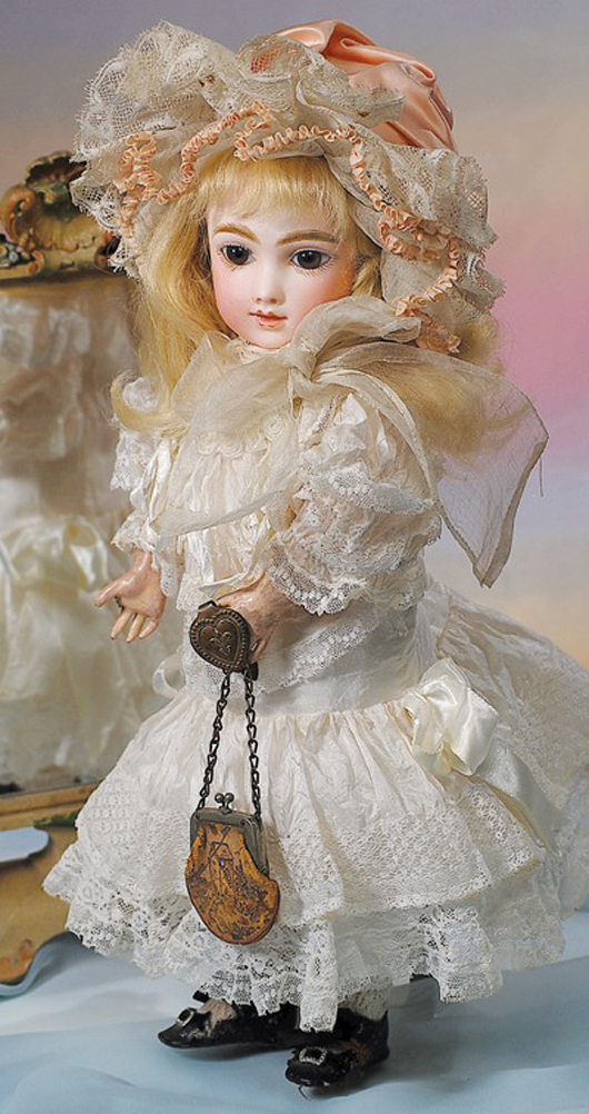 Full-length view of 16-inch A.T. French bisque bebe by Thullier, circa 1882, in white silk frock with lavish lace and ribbon trim and wearing a fancy pink silk bonnet and black leather shoes. Image courtesy of Frasher's Doll Auctions.