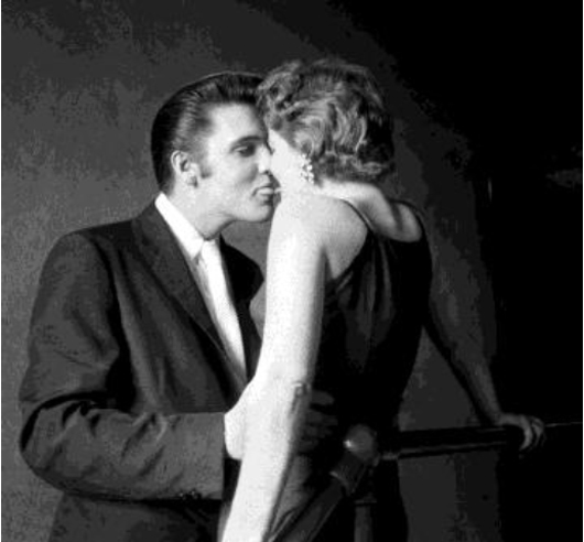 The Kiss, In the privacy of the narrow hallway under the fire stairs of the Mosque Theater (now the Landmark Theater), while other performers are on stage before 3000 fans in the audience, Elvis is concentrating on his date for the day. Mosque Theater, Richmond, Va. June 30, 1956. © Alfred Wertheimer. All rights reserved.