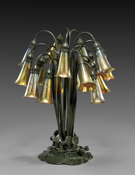 Tiffany Studios bronze and Favrile glass 18-light Lily lamp with splayed base comprised of overlapping lily pads rising to long gathered stems 22 1/4 inches high, signed 'Tiffany Studios New York 383,' the shades signed 'L.C.T.' Estimate: $25,000-$35,000. Image courtesy of I.M. Chait.
