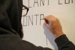 AKyle painting the title of his exhibit on the wall of the gallery. Artwork by Kyle Hughes-Odgers. Photograph courtesy Okazi Gallery.