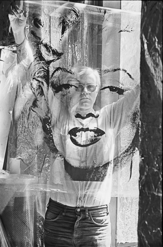 Andy Warhol holding an unrolled acetate of “Marilyn” in the Factory. Title: Warhol Holding Marilyn Acetate II Location: The Factory, New York City Medium: Silver Gelatin Fiber Print Edition: 60 with 7 Artist Proofs Size: 24 x 20 inches Executed: 1964  Printed: 2010 Copyright 2010 William John Kennedy / Courtesy of Kiwi Arts Group