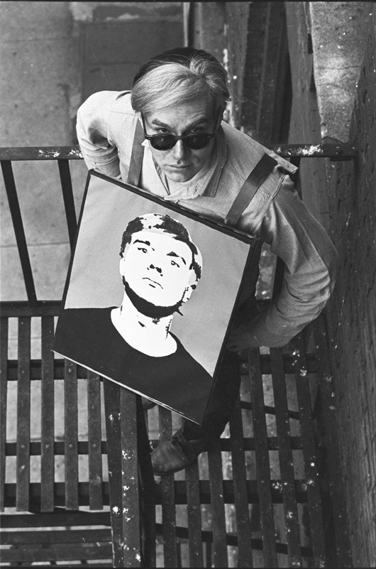 Andy Warhol with “Self Portrait” mounted on homemade sandwich board on fire escape at the Factory. Title: Warhol with Self Portrait SB, Factory Fire Escape II Location: The Factory, New York City Medium: Silver Gelatin Fiber Print Edition: 60 with 7 Artist Proofs Size: 20 x 16 inches Executed: 1964  Printed: 2010 Copyright 2010 William John Kennedy / Courtesy of Kiwi Arts Group
