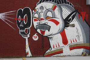 Yok’s character interacts with James Reka’s masked creature. Mural by Yok. Photo by Kelsey Savage.