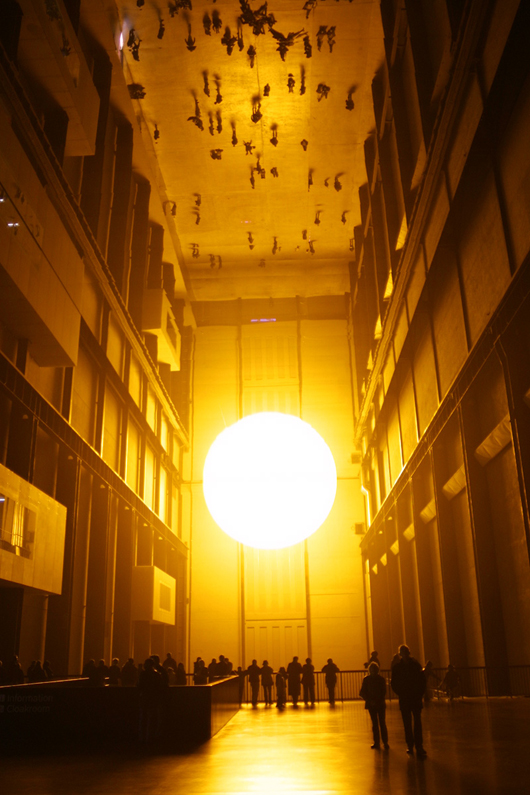 Olafur Eliasson's better-known installations include 'The Weather Project,' 2003, at Tate Modern in London. Eliasson used humidifiers to create a fine mist in the air via a mixture of sugar and water, and installed a semicircular disc composed of hundreds of monochromatic lamps that  radiated yellow light. Photo by Thomas Pintaric, licensed under the Creative Commons Attribution-Share Alike 3.0 Unported license.