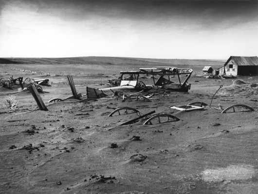 An automobile and farm equipment are buried by dust storms in a barnyard at Dallas, S.D., in May 1936. U.S. Department of Agriculture image, courtesy of Wikimedia Commons.