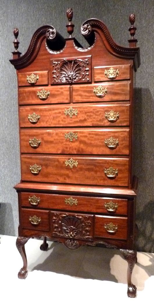 The height of the American highboy can be seen next in this Chippendale example from Philadelphia, circa 1750-1780. Philadelphia was the wealthiest city in the Colonies in mid-century and its highboys reflected the status. This one, like the best of the bunch, has matching carved drawers in the upper and lower cases with an open bonnet top centered by an urn and flame finial flanked by floral rosettes and dentil molding. 