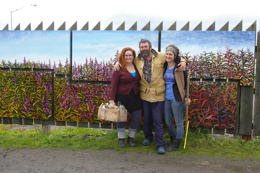 Dan Coe, center, stands with the assistants who helped him paint the fireweed mural, Karen Simpson, left, and daughter Rachel Coe, right. The six-panel mural shows the progression of fireweed from flower to fluff over the growing season. Image by Michael Walsh.
