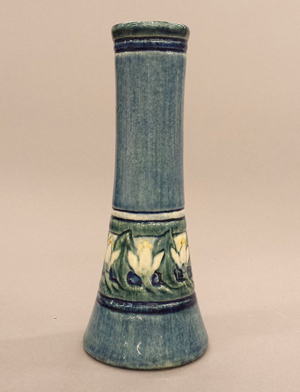 Newcomb College bud vase, decorator Marie De Hoa LeBlanc, potter Joseph Meyers; circa 1907, white clay body with blue, green and yellow glossy glaze with daffodil decoration. Impressed on bottom NC, JM, W; marked in blue MHLeB, BZ-90. 6 3/4in h x 2 3/4in dia. Estimate $3,000-$4,000. Quinn's Auction Galleries Image.