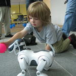 A child plays with a Sony AIBO ERS-7 robot dog. Image Stuart Caie. This file is licensed under the Creative Commons Attribution 2.0 Generic license.