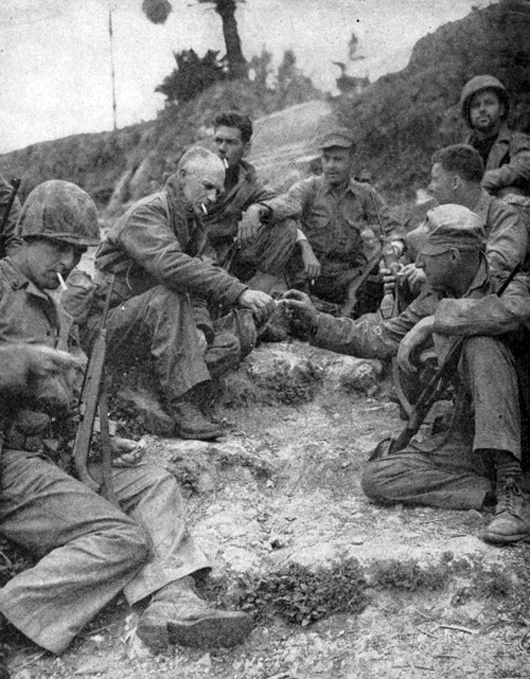 Ernie Pyle (second from left) shares a cigarette with U.S. Marines on Okinawa in 1945. Image courtesy of Wikimedia Commons.