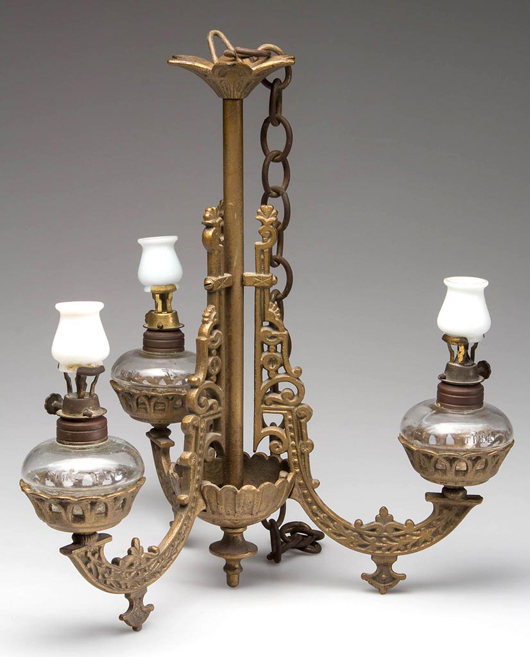 Just over 10 inches tall, this rare hanging cast-iron miniature triple-arm chandelier lamp, with the correct opaque glass chimney-shades, sold for $8,625. Jeffrey S. Evans & Associates image.