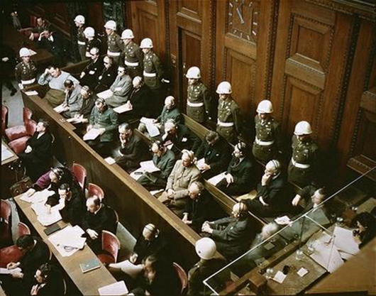 Rare color photo of the trial at Nuremberg showing the defendants guarded by American Military Police. Image courtesy of Wikimedia Commons.