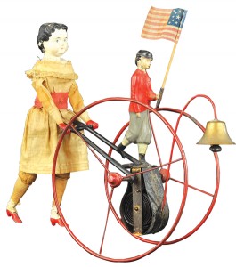 Girl Pushing Hoop toy, manufactured by George Brown, circa 1890s, depicts William Goodwin girl in cloth dress ‘pushing’ a tin hoop toy, with Suffragette figure holding American Flag at center, est. $10,000-$12,000. Bertoia Auctions image