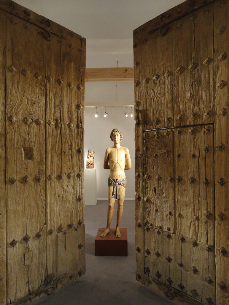 A late 14th-century wooden reliquary figure of St. Sebastian on the stand of Belgian dealer Pieter De Backker at the Masterpiece Fair where it was priced at €135,000 ($150,300). The 15th-century Spanish wooden doors were for sale at €37,500 ($41,750). Image Auction Central News.