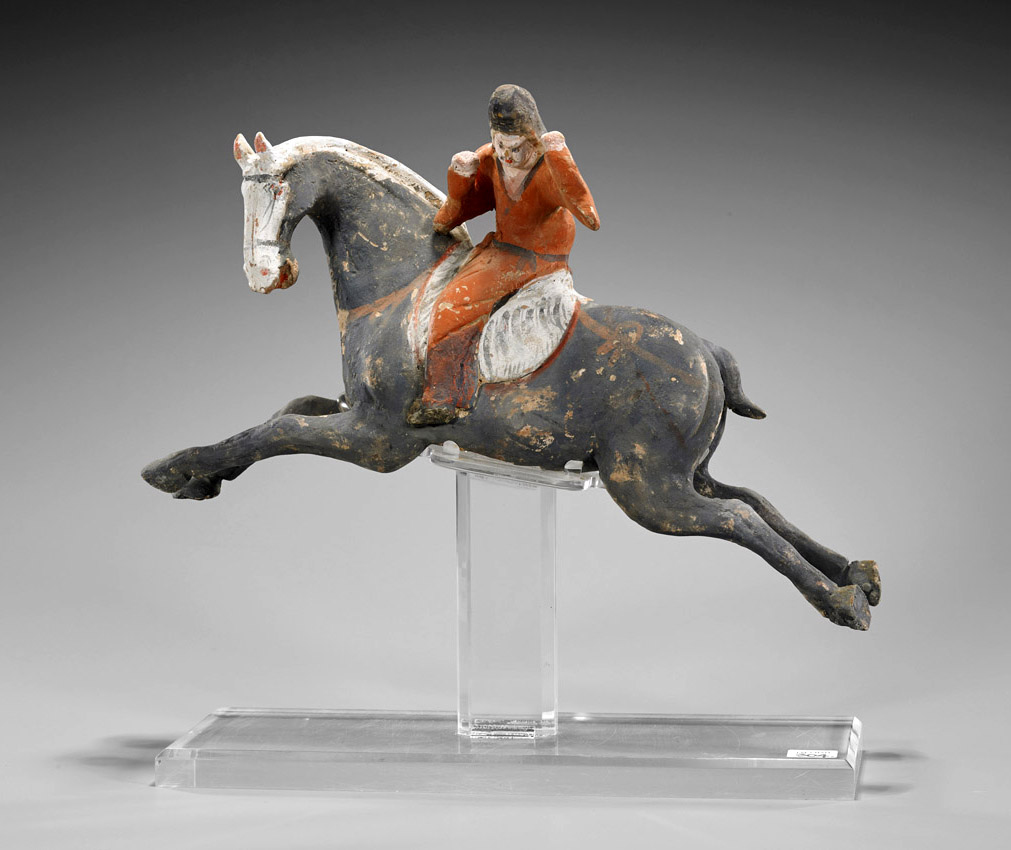 Chinese Tang Dynasty painted pottery polo player dressed in red with a black cap and seated atop a leaping gray horse, 16in long, on a Lucite stand. Estimate $800-$1,200. I.M. Chait image