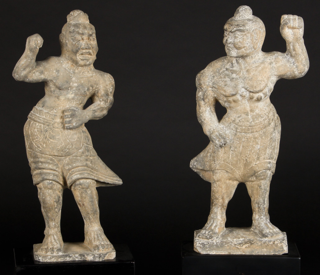 Lot 181 – Pair of Chinese Tang Dynasty dvarapala carved stone sculptures (A.D. 618-907). Two muscular guardian figures of dark gray stone, 25 inches high. Estimate: $30,000-$40,000. Material Culture image
