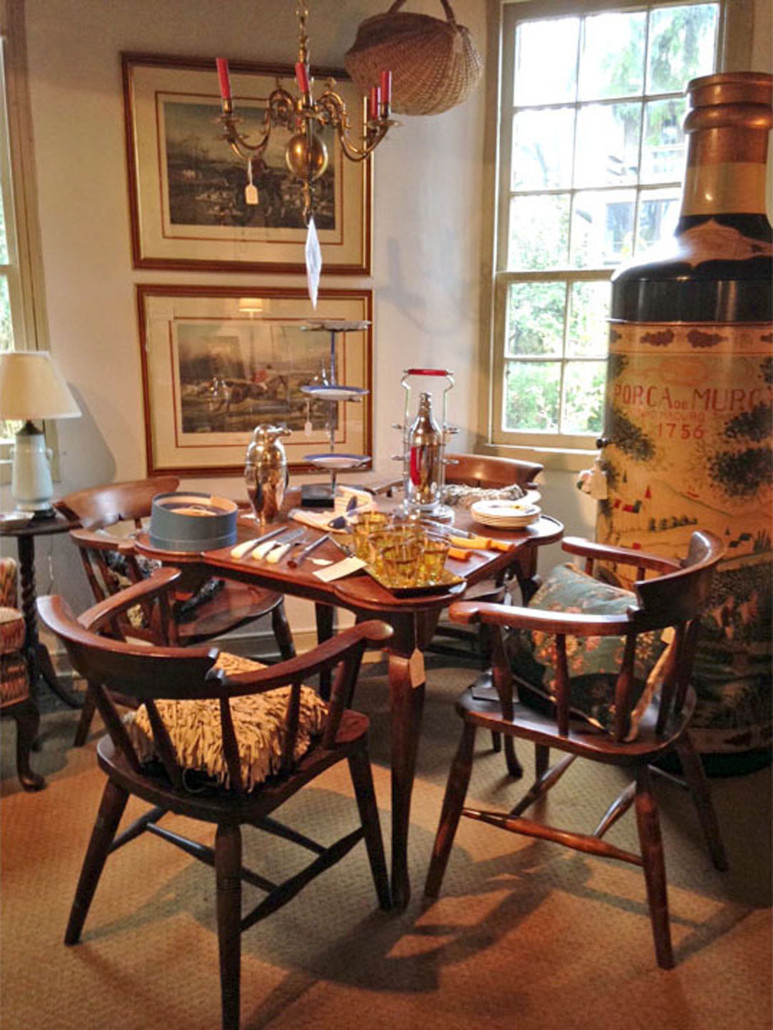 A table and chairs, barware and framed prints displayed in the annex of Sally Goodman’s New Hope antiques store