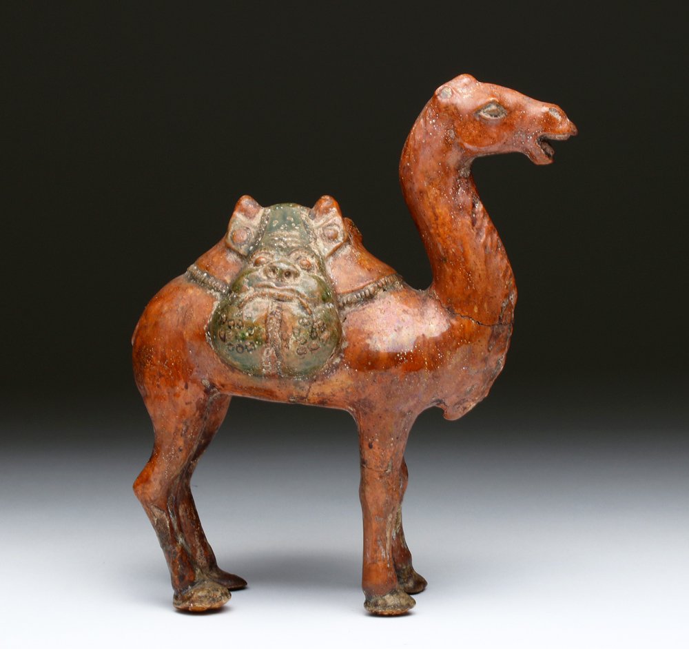 China, Tang Dynasty, sancai glazed hollow dromedary camel with saddle and saddle bags depicting a grotesque face with bulging jowls. Estimate: $1,800-$2,500. Artemis Gallery image