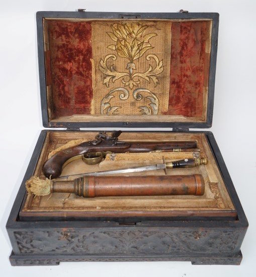 Spanish pirate chest intricately carved with an antique tapestry mount at the inside of the box, containing pistol with cross and skull bones mount. Sold for $5,750
