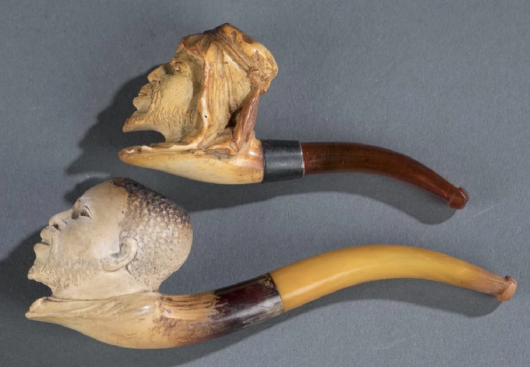 Two Meerschaum pipes, one depicting a Black American head, with collar and tie; the other depicting a North African man’s head, est. $100-$200 the pair