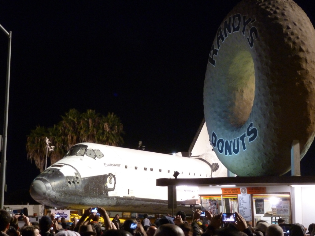 The Space Shuttle Endeavour pictured with the Los Angeles landmark Randy’s Donuts as the retired spaceship proceeded to the California Science Center on October 12, 2012. Ground was broken for a new museum devoted to Endeavour on June 1. Image courtesy of Wikimedia Commons, photo credit Bluesnote. Shared under the Creative Commons Attribution-Share Alike 3.0 Unported license