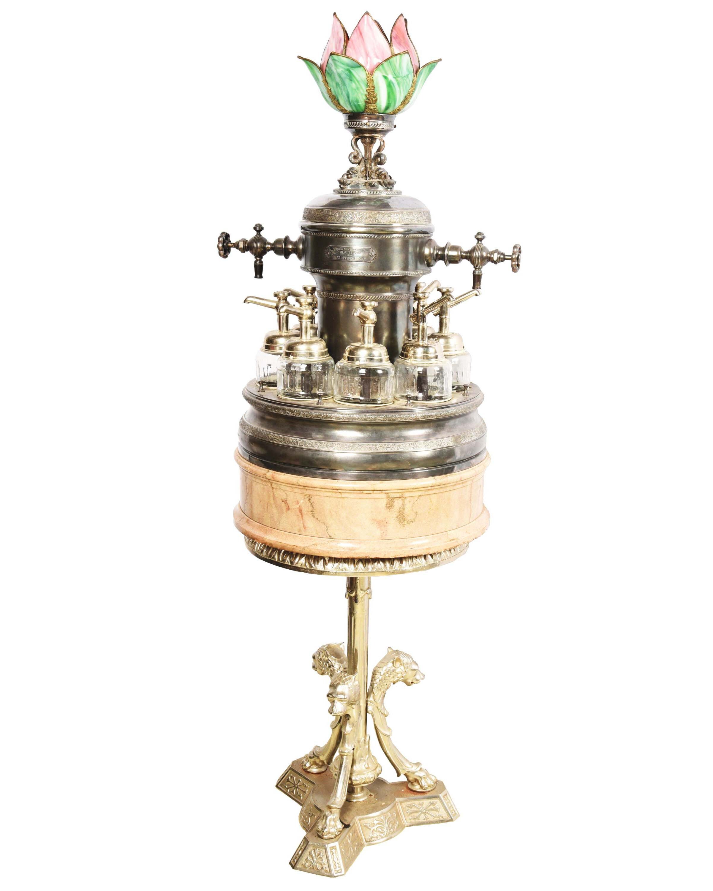 Soda fountain syrup dispenser made around the turn of the 20th century by American Soda Fountain Co., Philadelphia. Original double tap with six original glass fountain flavor dispensers. Lighted leaded-glass tulip-form finial. Estimate $3,000-$6,000