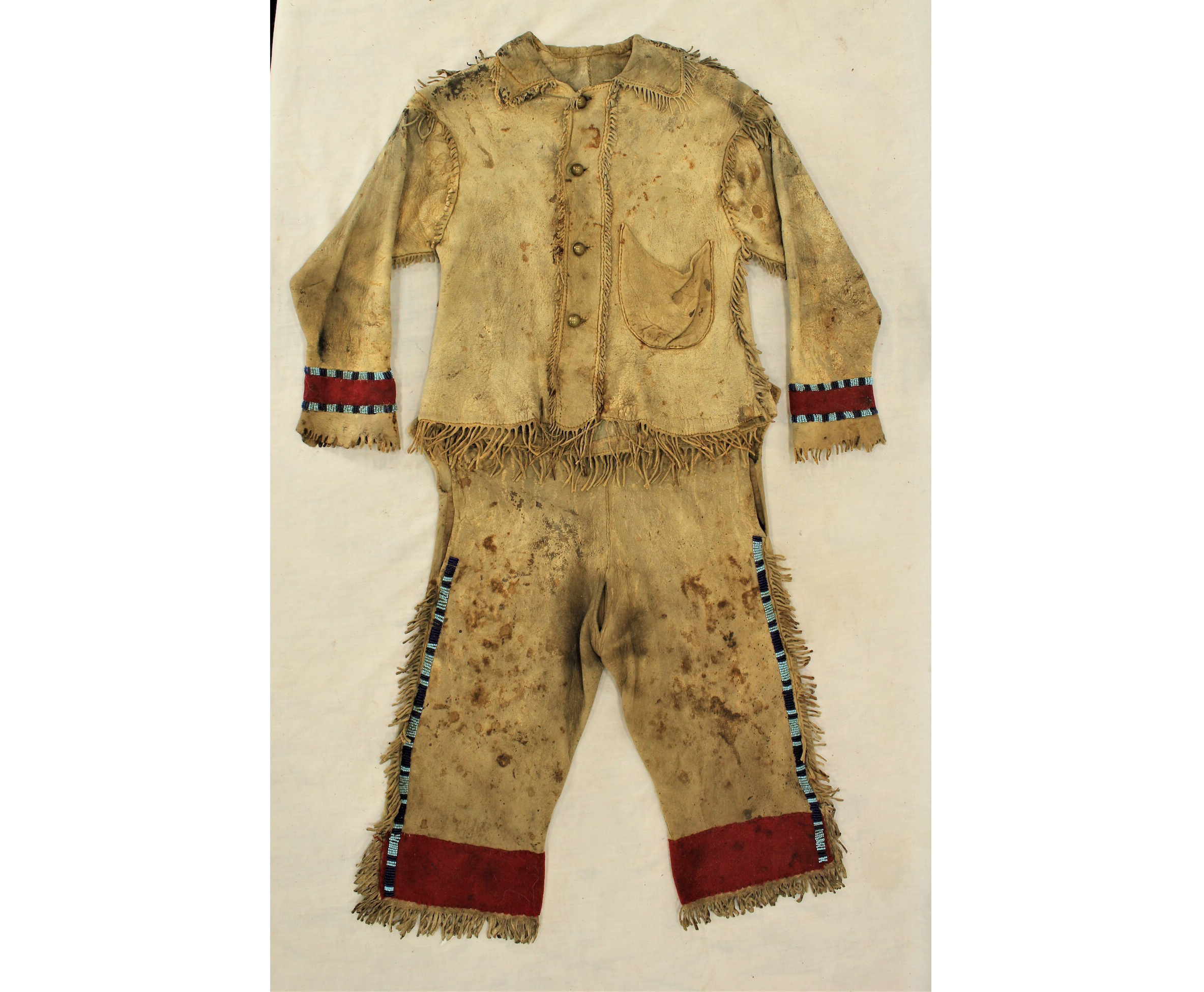 Phenomenal 1880s Crow Indian child’s buckskin shirt and pants. Fringed throughout, with trade-cloth cuffs and early cobalt blue and robin’s-egg blue beads. Est. $2,000-$4,000