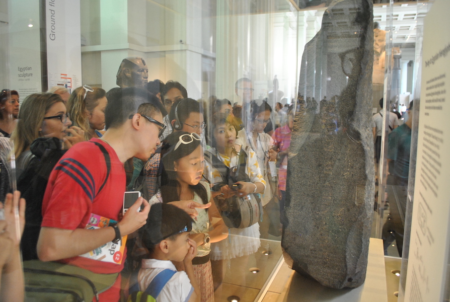 Visitors crowd around the Rosetta Stone at the British Museum in August 2014. The historic artifact is one of the most popular displays at the museum. Image courtesy of Wikimedia Commons, photo credit ProtoplasmaKid. Shared under the Creative Commons Attribution-Share Alike 4.0 International license.