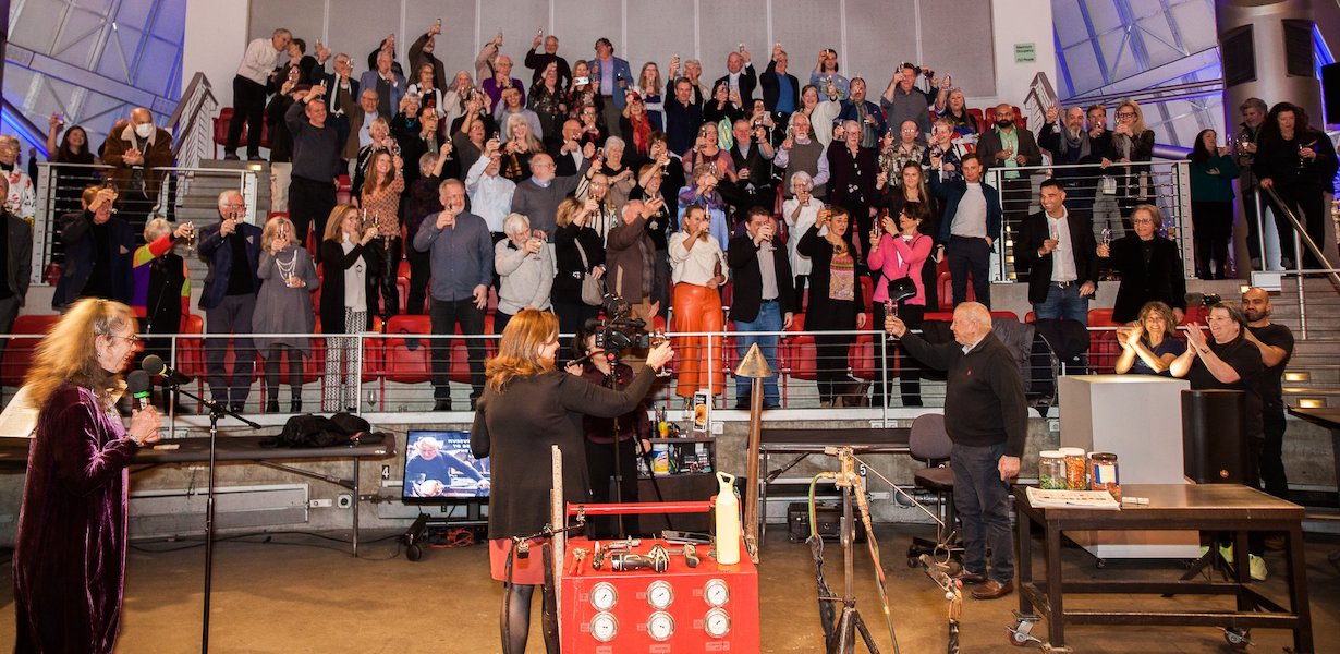Dozens of attendees of the March 4 Museum of Glass celebration of Lino Tagliapietra’s career raise a toast to the artist, who is retiring to his home country of Italy. Image courtesy of the Museum of Glass. Photo by Pavel Verbovski.