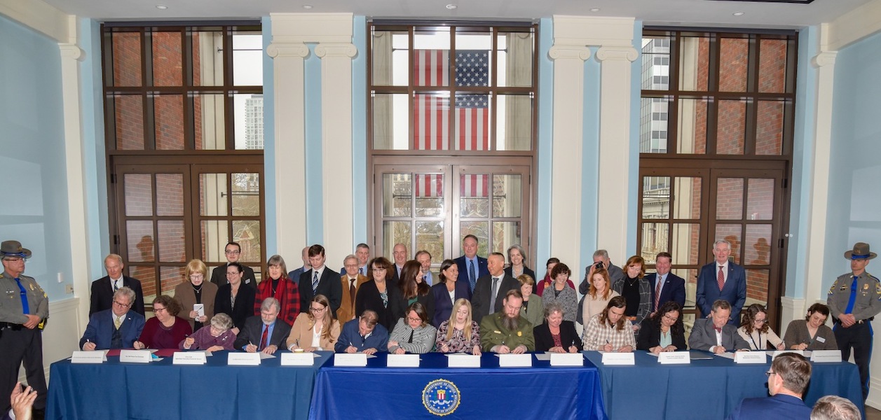Members of the investigation and prosecution teams who helped recover the stolen objects look on as representatives from the victim institutions sign repatriation documents, formally accepting custody of their recovered artifacts. Image courtesy of the Federal Bureau of Investigations (FBI)